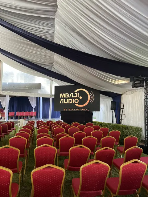 Tent with rows of red chairs and a Mbaji Audio sign